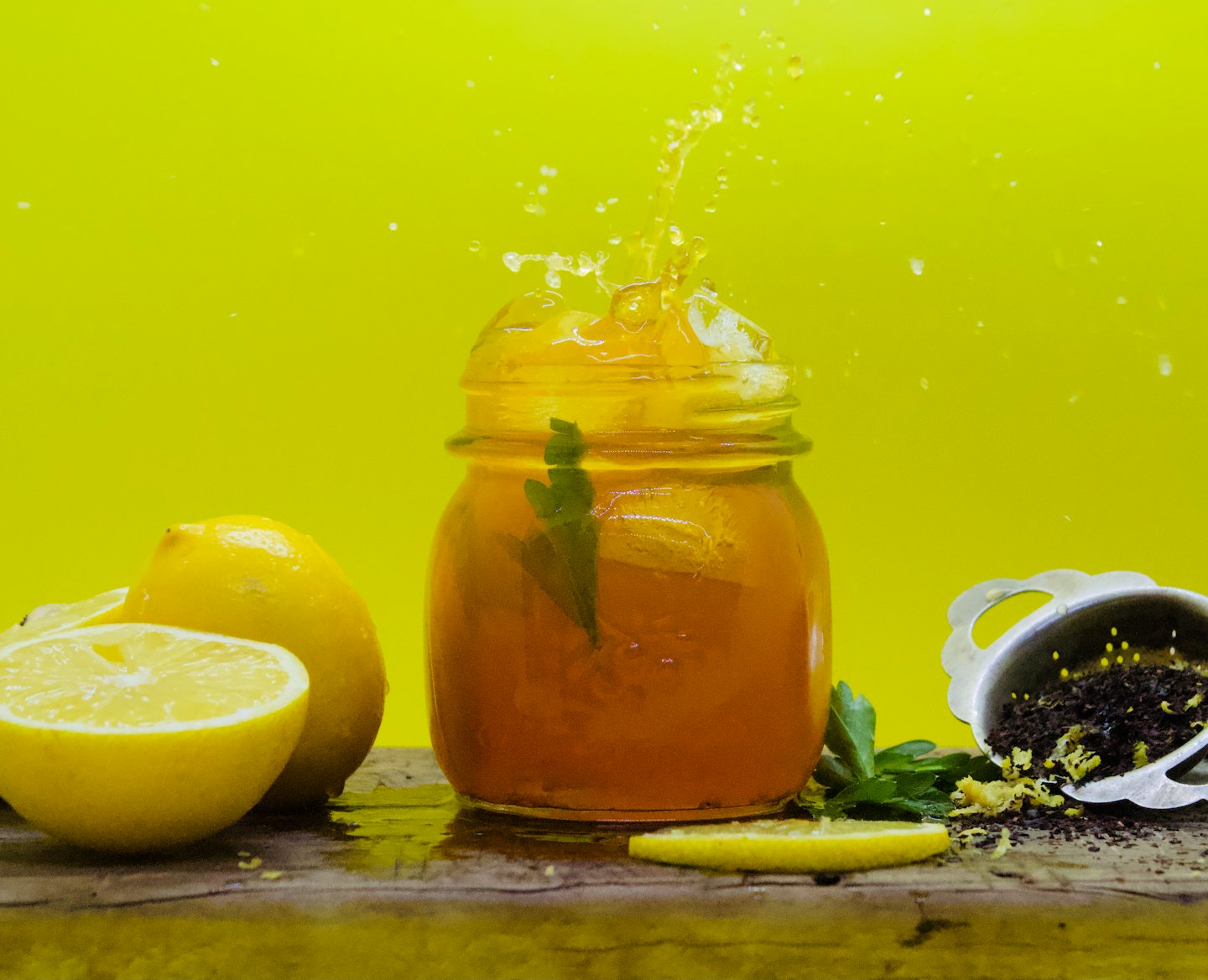 Iced tea splashes from a glass jar surrounded by lemons.