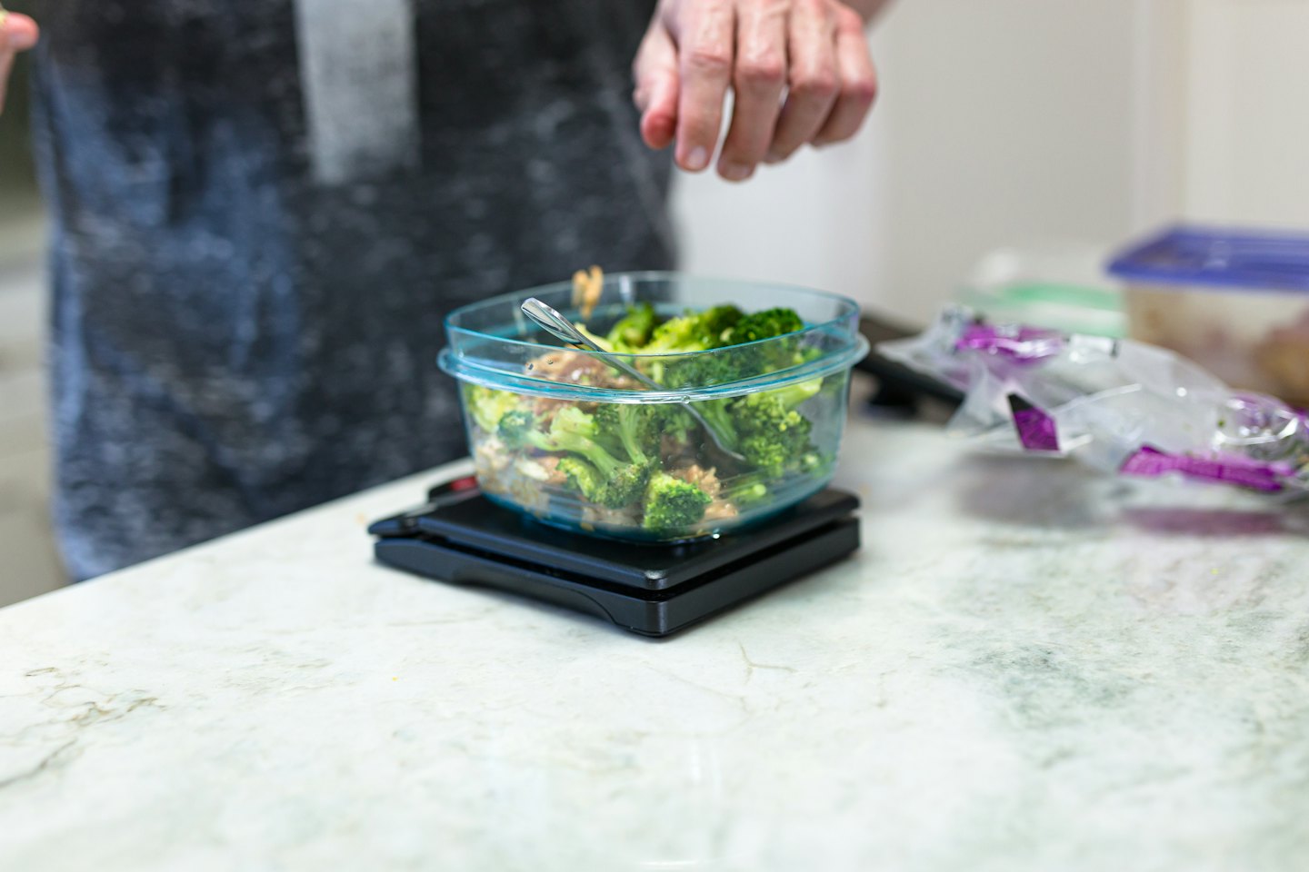 Person weighing broccoli and rice for meal prep.