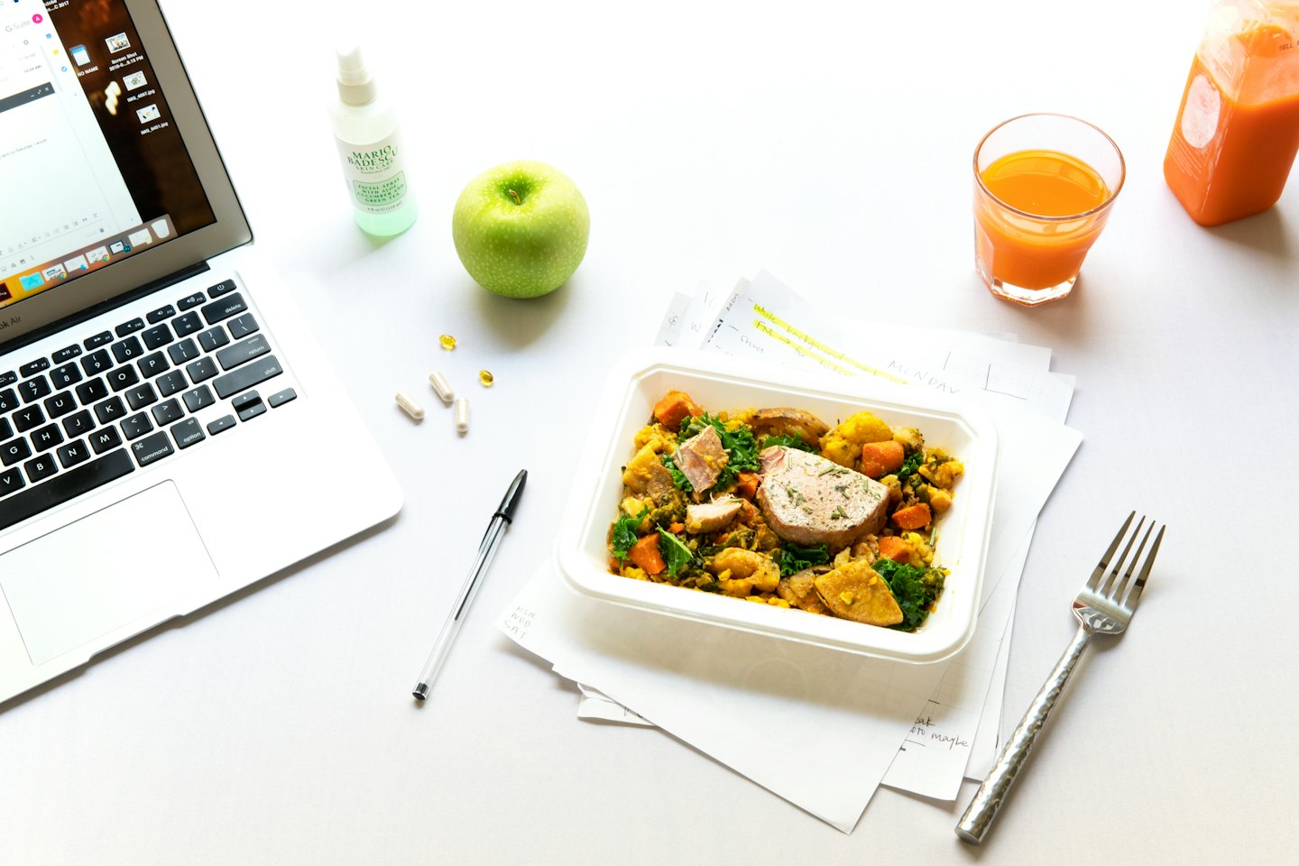 Healthy lunch and work supplies on a white desk.